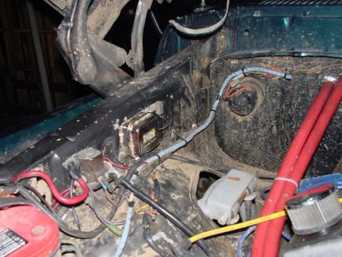 1979 Ford Bronco - The engine bay of a vehicle is cluttered with wiring and components, including a red battery and a black box with a yellow label.