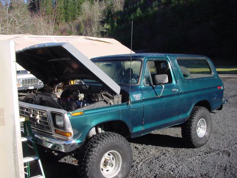 1979 Ford Bronco - A green 1979 Ford Bronco sits with its hood up, revealing the engine bay. Another vehicle is parked behind it.