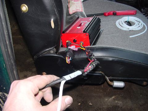 1979 Ford Bronco - A red ignition system component is placed on a car seat, connected by wires, with a hand holding a cable nearby.
