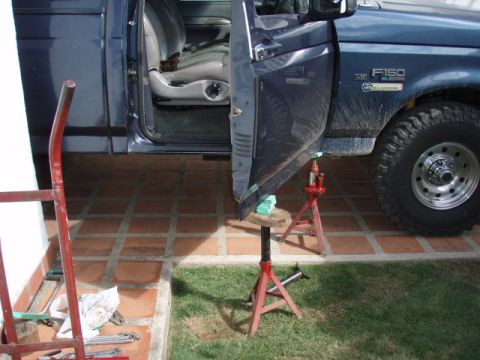 1995 Ford F-150 - Blue Ford F-150 XL pickup with its driver's door removed and propped upright on red jack stands and a bottle jack over a tile patio. The st…