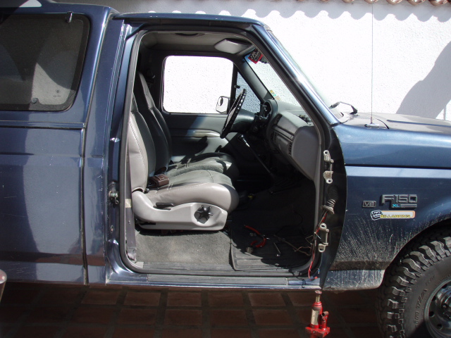 1995 Ford F-150 interior showing seats, dashboard, and open driver's door. F150 badge visible on fender