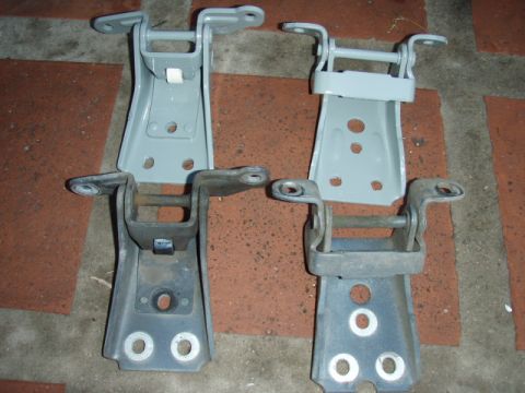 1995 Ford F-150 - Two pairs of automotive door hinges are displayed on a textured surface, with one set appearing newly painted.