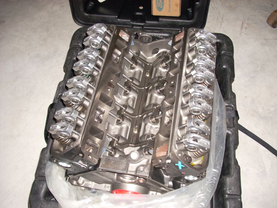Ford V8 engine block with valve covers removed, showing rocker arms and springs. It's in a black plastic case