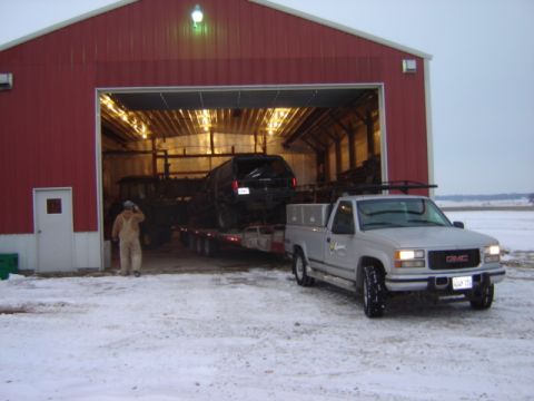 1992 Ford Bronco - A silver GMC pickup truck is parked in front of a red barn, with a trailer carrying a black SUV inside.