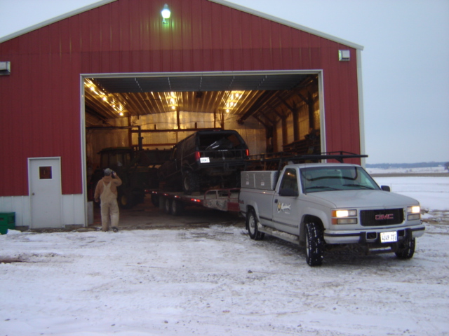 Silver GMC pickup truck parked in front of a red barn with a trailer carrying a black SUV