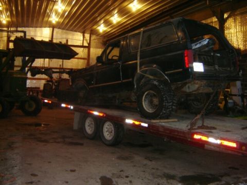 1992 Ford Bronco - A black 1992 Ford Bronco is loaded onto a trailer inside a barn, with a tractor assisting.