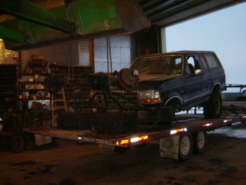 1992 Ford Bronco - 1992 Ford Bronco loaded onto a trailer inside a workshop, with extra parts visible.
