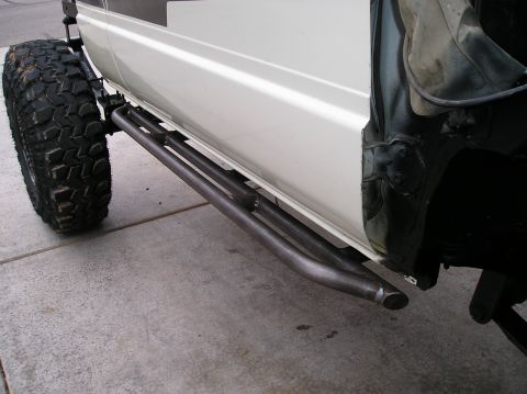 1986 Toyota Hilux - Side view of a white pickup's lower body showing a custom fabricated tubular steel rock slider/rock rail mounted below the door, with an op…
