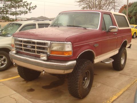 1992 Ford Bronco - A lifted maroon 1992 Ford Bronco with a white top is parked outside on a wet day.