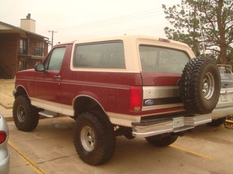 1992 Ford Bronco - Driver-side rear three-quarter view of a lifted burgundy-and-tan Ford Bronco with a white removable hardtop and an Oklahoma plate, parked a…