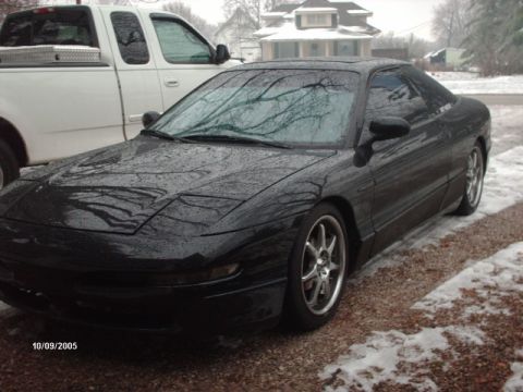 1995 Ford Probe - A black coupe is parked next to a white pickup truck on a snowy day.