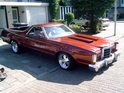1972 Ford Ranchero - A shiny, dark red Ford Ranchero is parked on a paved driveway in front of a house. The vehicle has chrome wheels and hood scoops.