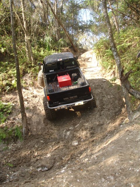 1989 Ford Bronco - An SUV navigates a dusty, uphill trail surrounded by foliage.