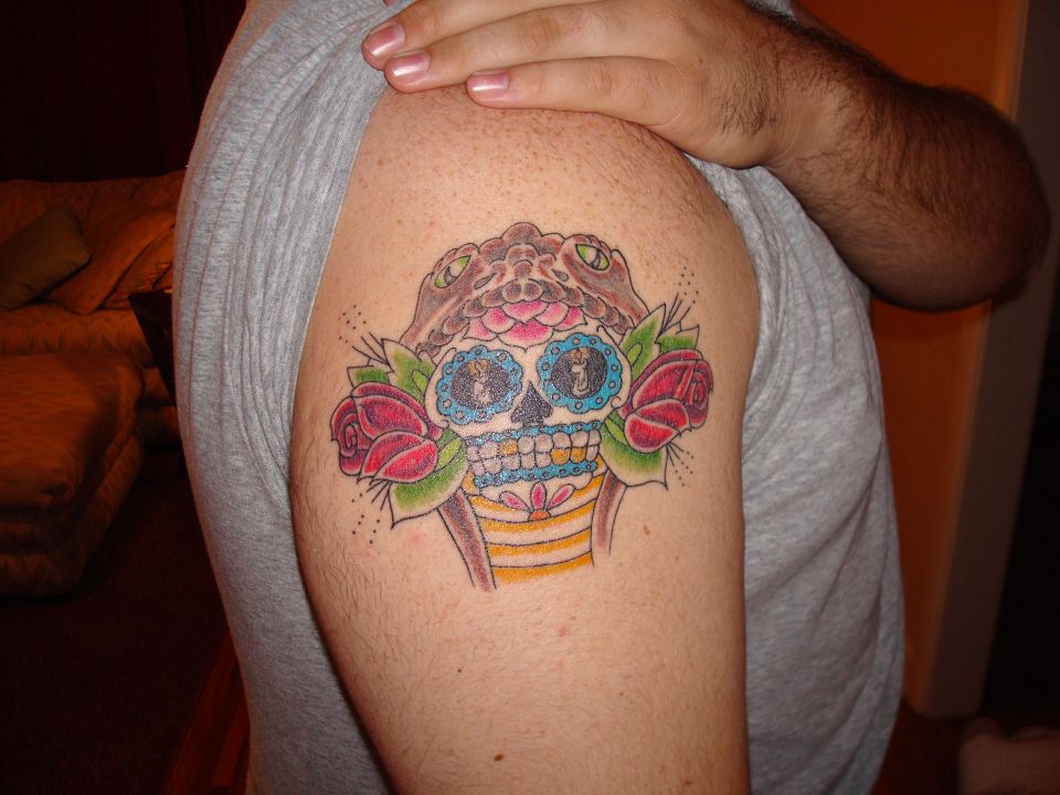 Tattoo of a sugar skull with snakes and roses on a person's arm