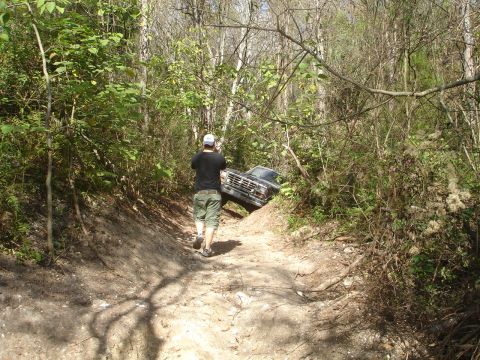 1989 Ford Bronco - A man walks up a wooded trail as a Ford Bronco is partially stuck on the embankment.