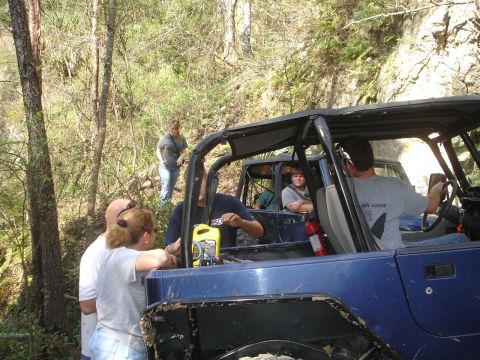 1989 Ford Bronco - People gather around a blue off-road vehicle on a wooded trail, with another vehicle visible behind it.