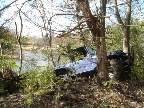 1989 Ford Bronco - This vehicle appears to be stuck in a wooded area, leaning against trees with a lake in the background.