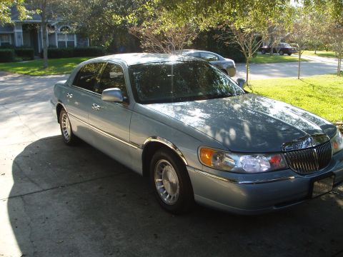 1998 Lincoln Town Car - A light blue 1998 Lincoln Town Car is parked in a driveway with trees and a house in the background.