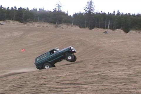 1979 Ford Bronco - A green 1979 Ford Bronco navigates a steep sand dune, demonstrating its off-road capabilities.