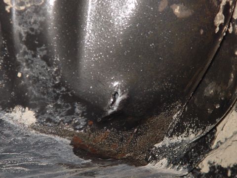 1979 Ford Bronco - A close-up view reveals a rusty hole on a dark, textured surface, possibly indicating damage or wear.