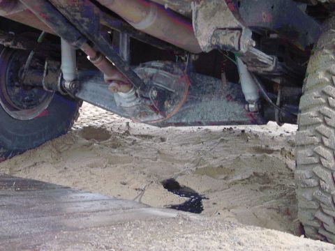 1979 Ford Bronco - The vehicle's undercarriage is visible, partially submerged in sand with a dark fluid leak.