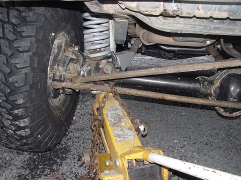 1979 Ford Bronco - Close-up view of a vehicle's undercarriage, showing suspension, a tire, and a jack supporting the frame.