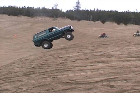 1979 Ford Bronco - Ford Bronco airborne over a sand dune, with ATVs in the background.