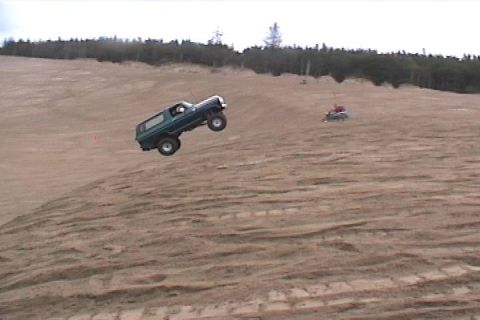 1979 Ford Bronco - A 1979 Ford Bronco takes flight over a sandy incline, with another vehicle visible in the distance.