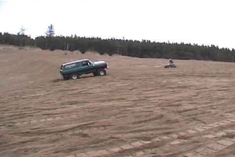 1979 Ford Bronco - A green 1979 Ford Bronco navigates sandy terrain, with an ATV visible in the distance.
