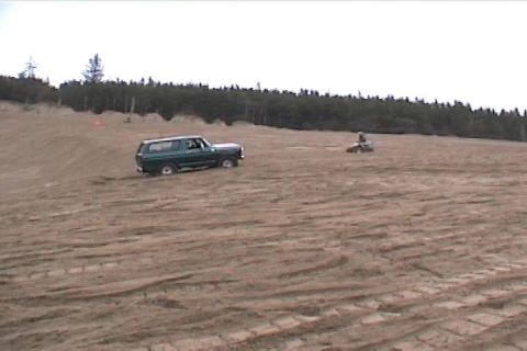 1979 Ford Bronco - SUV and ATV on a sandy terrain with trees in the distance.