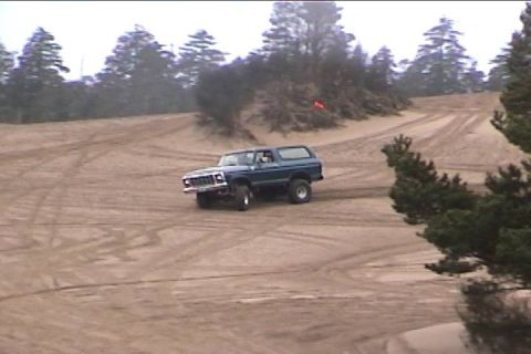 1979 Ford Bronco - A blue SUV navigates a sandy terrain with tire tracks visible on the ground.