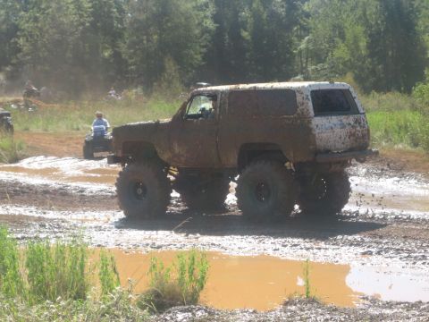 1994 Ford Bronco - This heavily modified SUV is covered in mud while navigating a challenging off-road course with other vehicles.