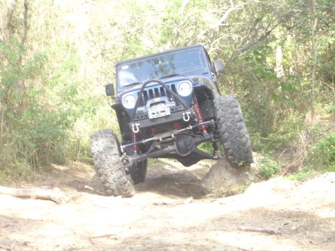 1989 Ford Bronco - Modified Jeep Wrangler tackling an off-road obstacle on a dirt path.