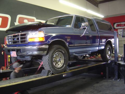 1996 Ford F-250 - A blue and gray Ford F-250 pickup truck is shown on a lift with its hood open in a garage setting.