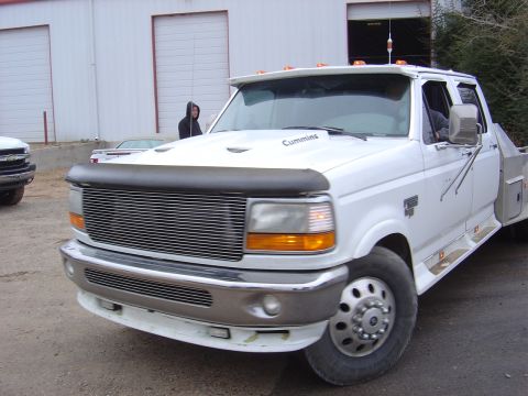 1996 Ford F-250 - A white Ford F-250 truck with a chrome grille and 'Cummins' badging is parked outside a short distance from a building.