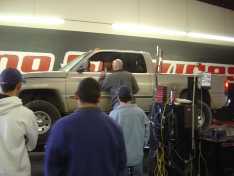 1996 Ford F-250 - A silver pickup truck is being worked on in a garage, with several people observing. The truck has a large exhaust pipe.