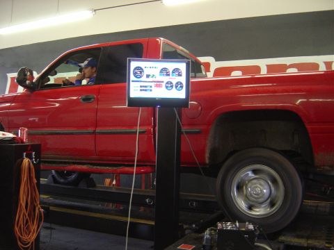 1996 Ford F-250 - A red pickup truck is being tested on a dynamometer, with a driver inside and a monitor displaying performance data.