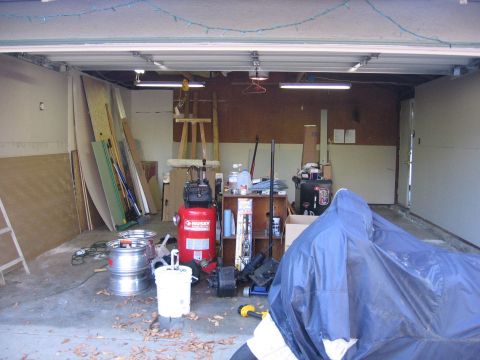 1989 Ford Bronco - A garage scene shows a vehicle covered by a blue tarp, surrounded by various tools and building materials.