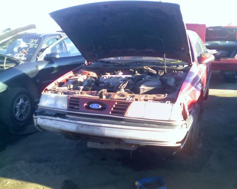 1993 Ford Taurus - This 1993 Ford Taurus is in a junkyard with its hood open, revealing the engine.