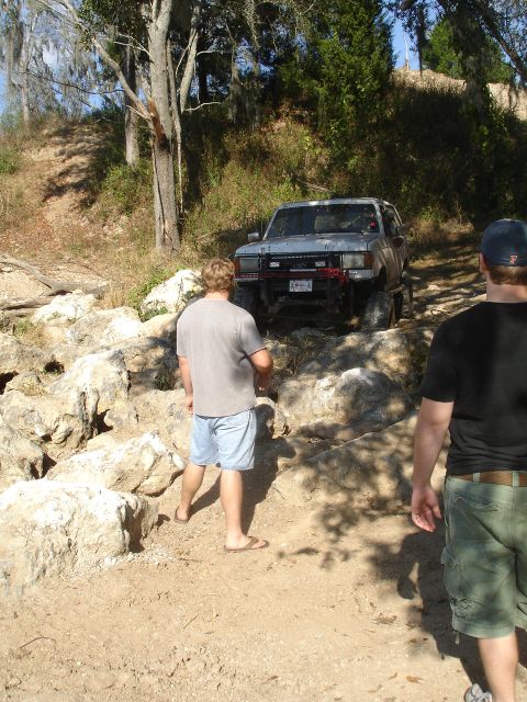 1989 Ford Bronco - An SUV navigates a rocky off-road course with two onlookers observing the challenging terrain.