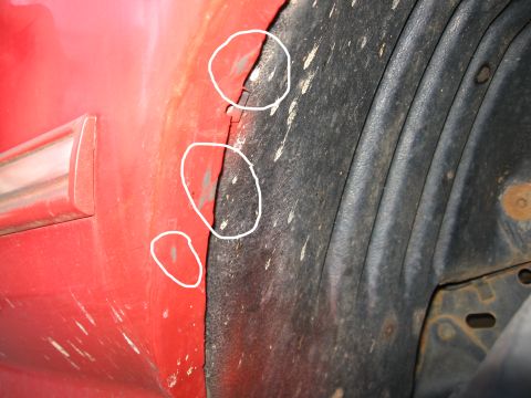 1995 Ford F-150 - Close-up of the front wheel-opening lip on a red pickup fender, with three white circles drawn on the image to mark rub marks and scuffed p…