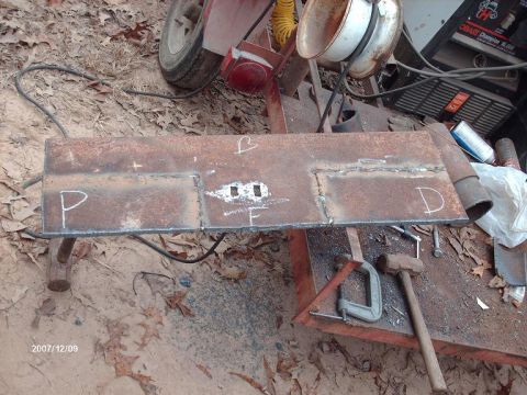1990 Ford F-150 - A fabricated metal component with chalk markings sits on a workbench, surrounded by tools and debris.