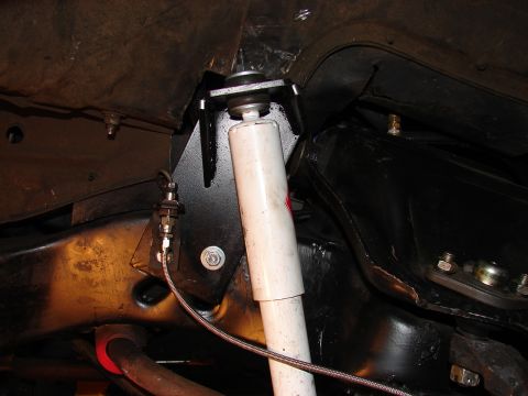 1973 Ford Ranchero - Underside view of a vehicle showing a newly installed white-bodied shock absorber mounted to a black-painted bracket welded to the frame. A…
