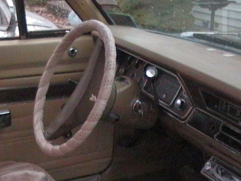 1990 Ford Bronco - The interior of an older vehicle shows a tan dashboard and a steering wheel with a fabric cover.