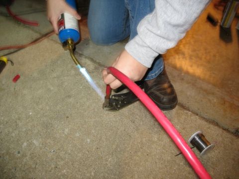 1995 Ford C-350 (Centurion Conversions) - A person is using a propane torch to heat a connector on a thick red cable, with a spool of wire nearby.