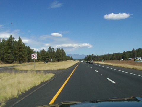 1995 Ford C-350 (Centurion Conversions) - A highway stretches through a landscape of trees and distant mountains under a blue sky with scattered clouds.