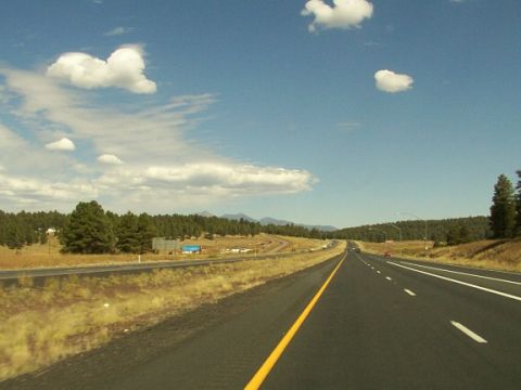 1995 Ford C-350 (Centurion Conversions) - A view from a highway shows distant vehicles and a landscape of trees and hills under a partly cloudy sky.