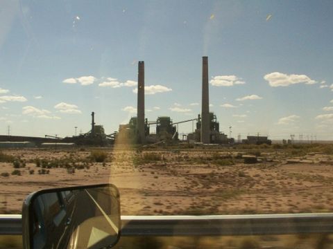 1995 Ford C-350 (Centurion Conversions) - A power plant with tall smokestacks is visible in the distance, seen through a vehicle's side mirror on a sunny day.