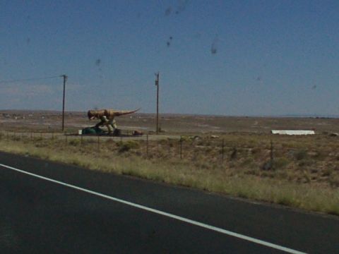 1995 Ford C-350 (Centurion Conversions) - A dinosaur statue stands beside a highway, a common roadside attraction in open country.