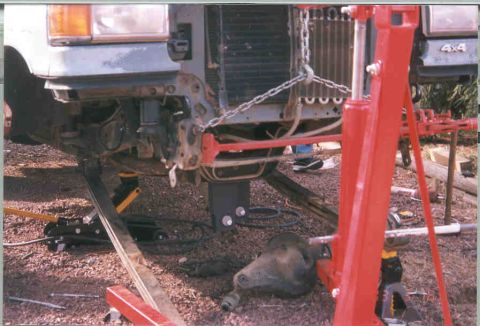 1991 Ford F-250 - Front suspension components of a truck are visible, supported by a red engine hoist and jack stands.